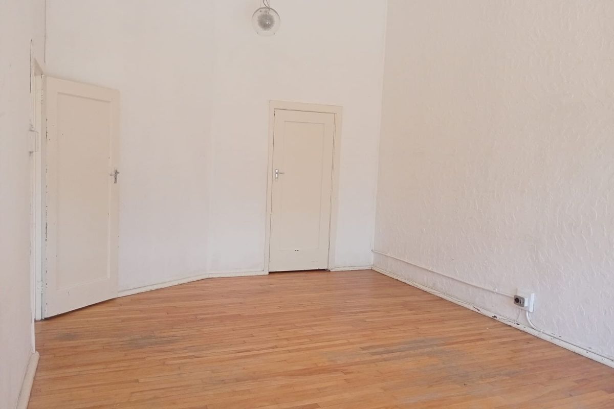 An empty bedroom featuring original timber flooring, white walls, and two internal doors, offering a blank canvas for renovation or interior design.