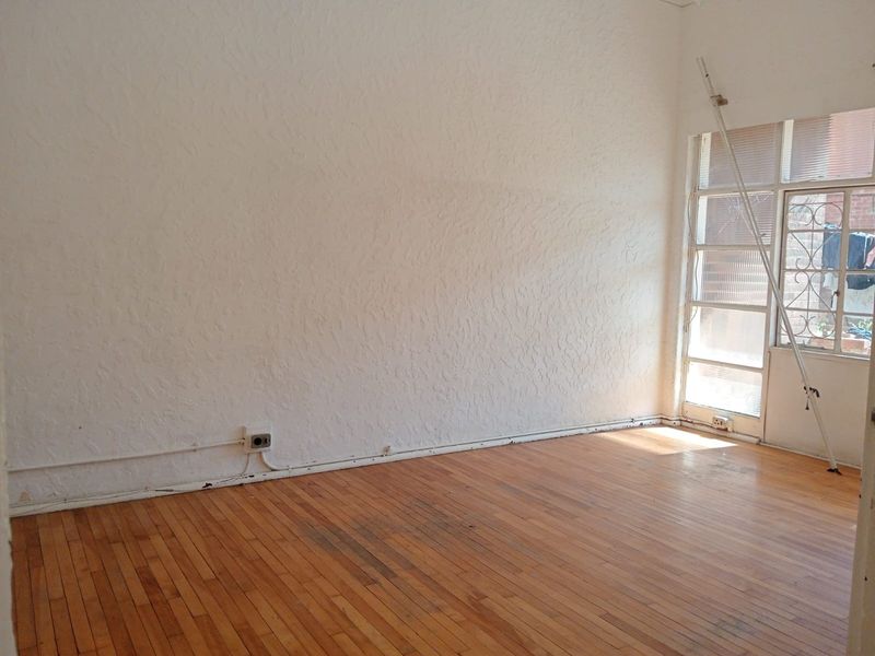 An empty living room featuring original timber flooring, textured walls, and a glass door leading to an outdoor area.