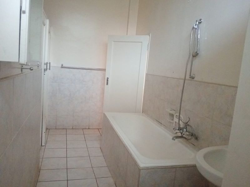 A functional bathroom featuring a built-in bathtub with a handheld shower fixture, tiled flooring, and wall-mounted towel rails.