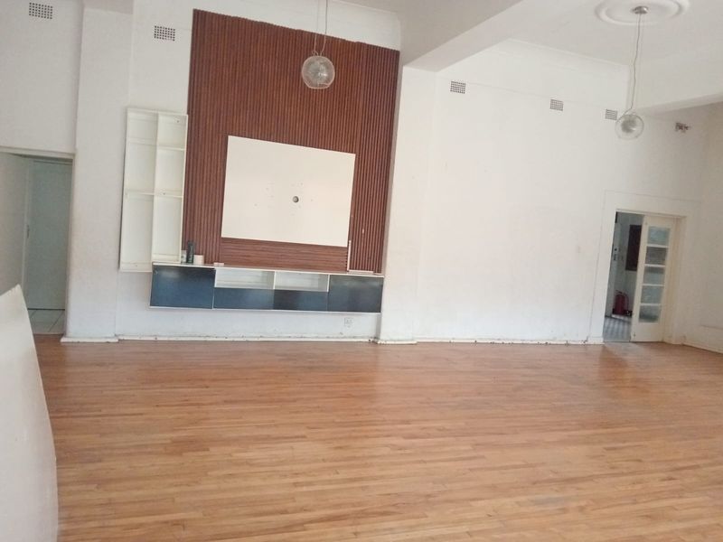 Spacious living area featuring timber flooring, a built-in media wall with decorative timber slats, and pendant lighting.