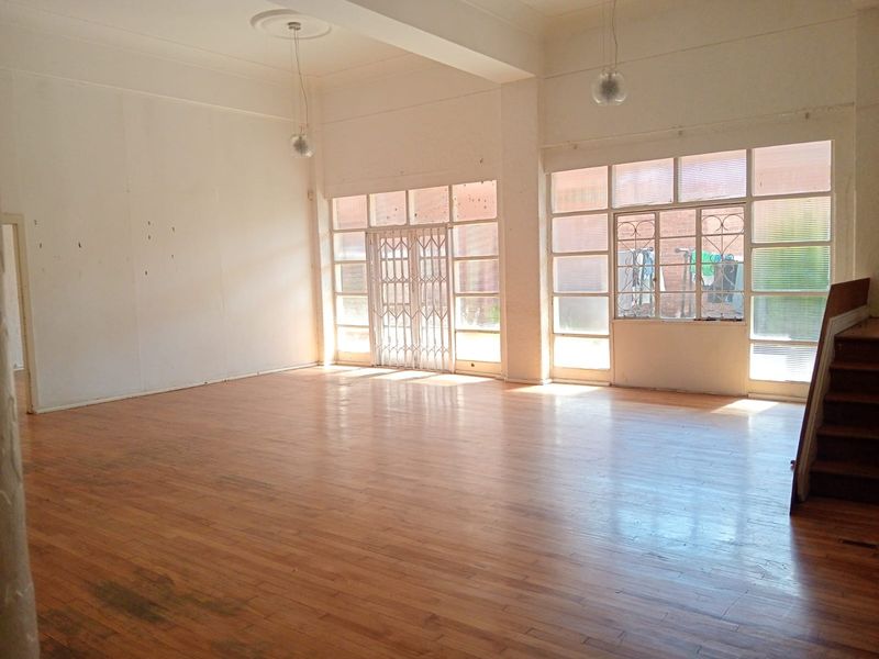Spacious, light-filled open plan living area featuring polished timber flooring, high ceilings, and large windows with security gates.