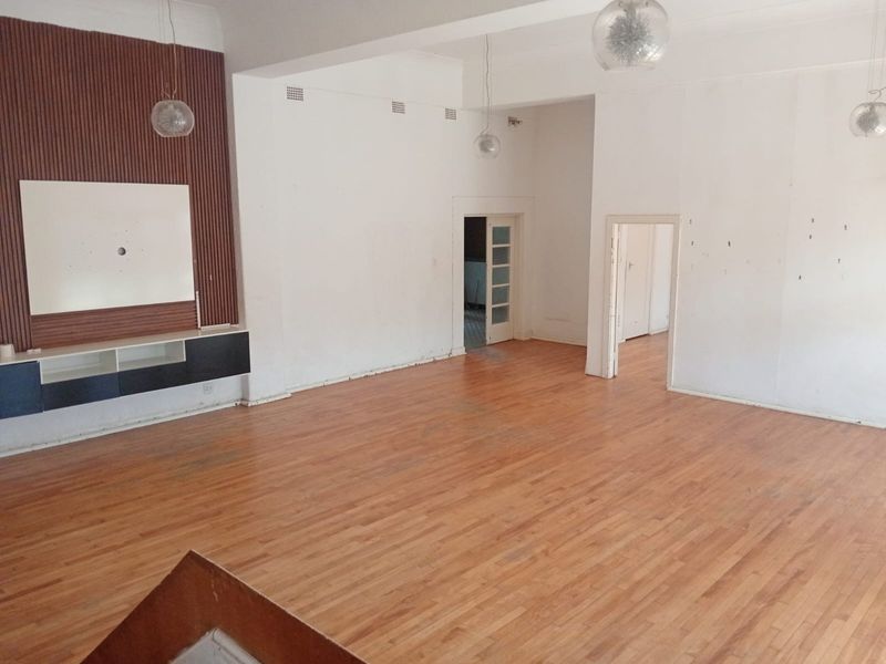 Spacious open-plan living area featuring polished timber flooring, a built-in media wall unit with timber slat detailing, and multiple access points to adjacent rooms.