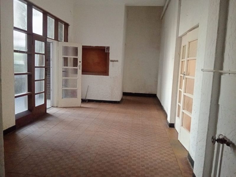 An empty, dated interior space featuring tiled flooring, multiple glass-paneled doors, and access to an outdoor area.