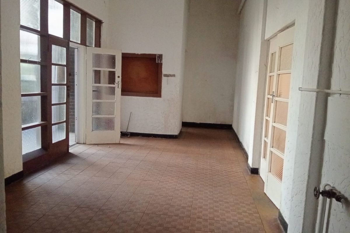 An empty, dated interior space featuring tiled flooring, multiple glass-paneled doors, and access to an outdoor area.