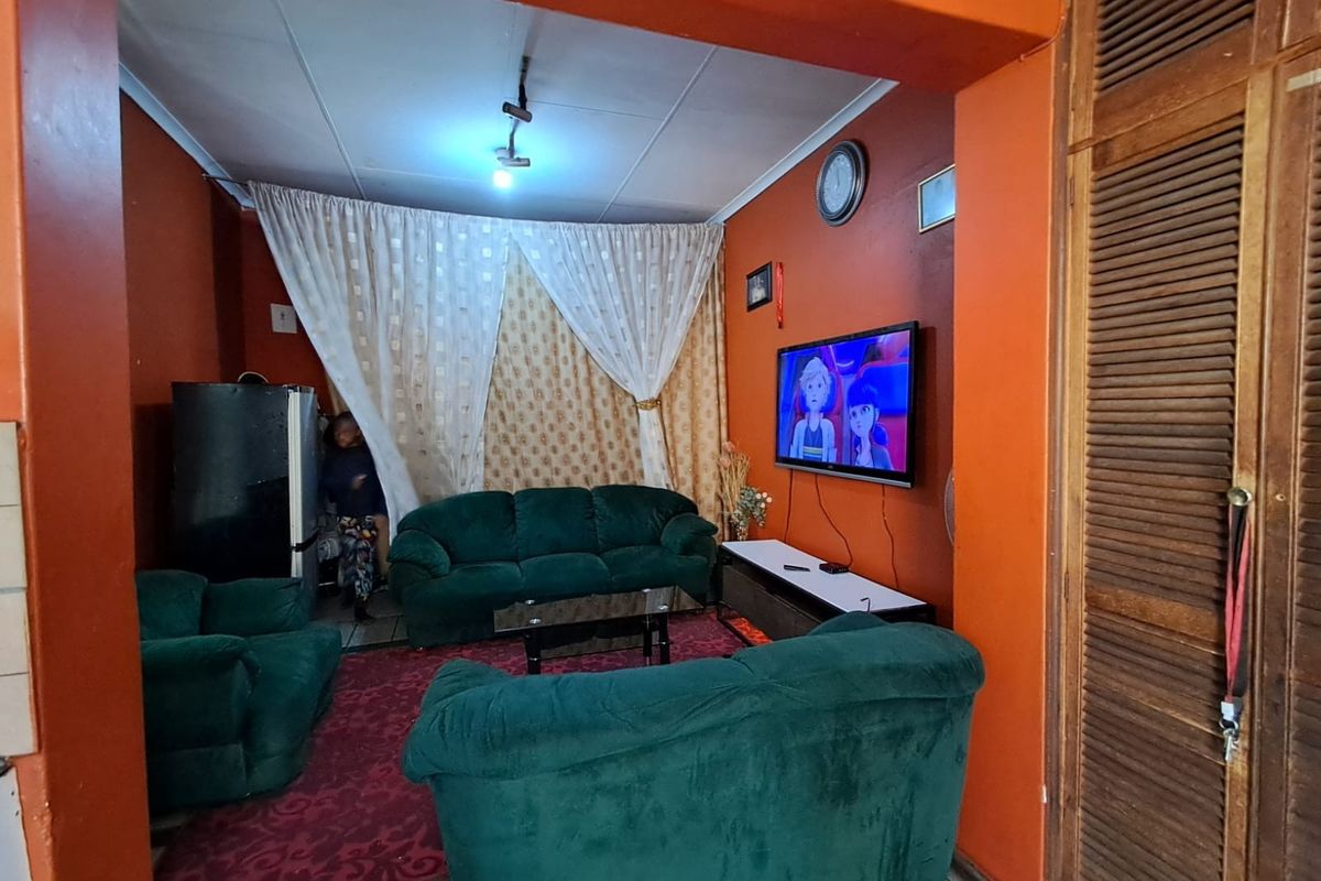 A living room featuring bold orange walls, tiled flooring, and built-in wooden louvered closet doors.
