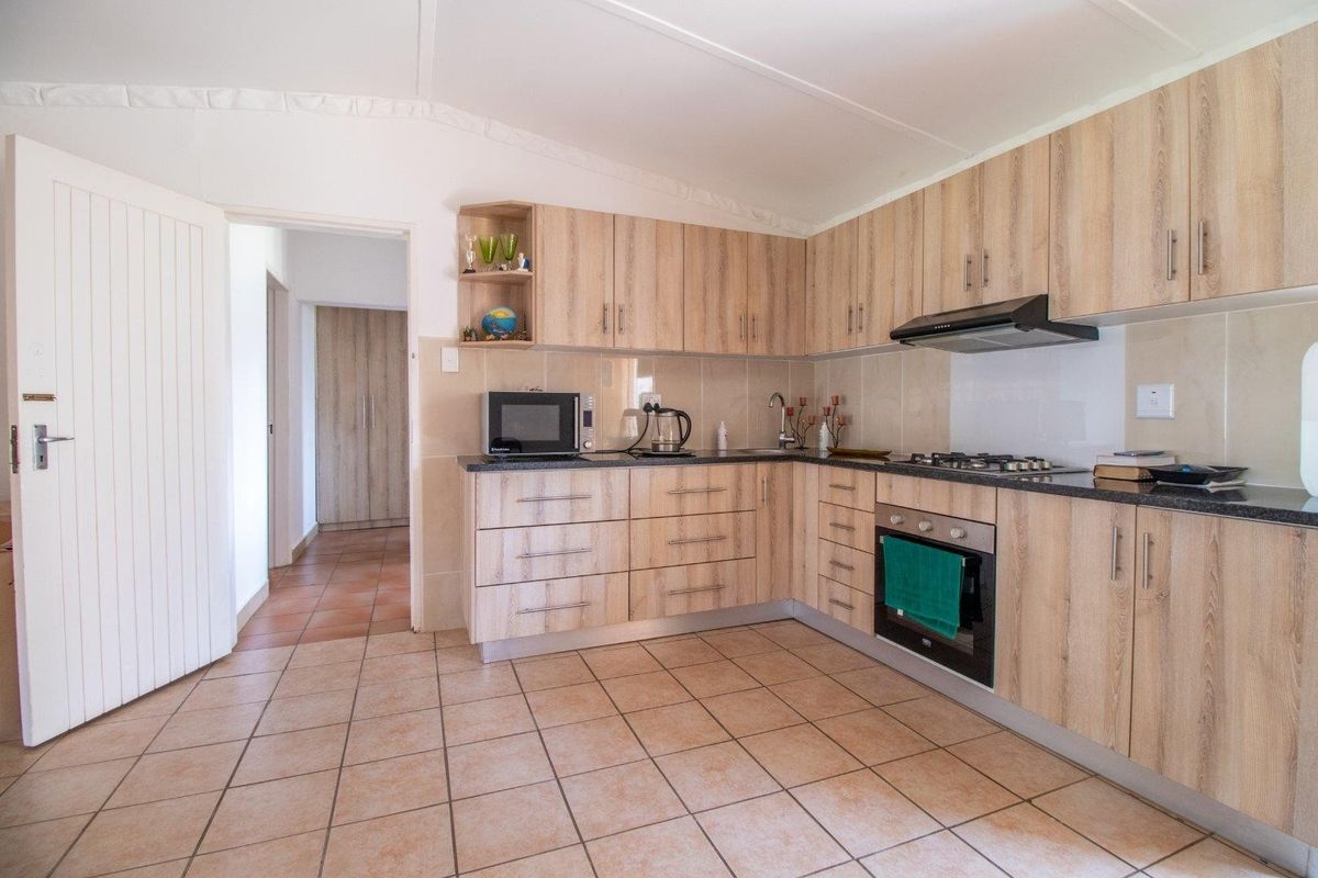 A functional kitchen featuring light wood-grain cabinetry, dark granite countertops, a built-in oven, gas hob, and extractor fan, with tiled flooring throughout.