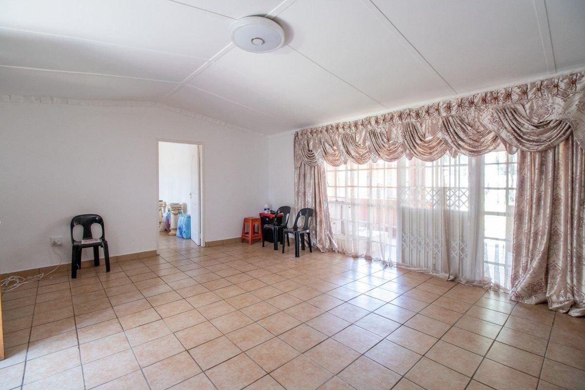 A spacious living room featuring neutral ceramic floor tiles, a ceiling-mounted light fixture, and large sliding glass doors with security gates.