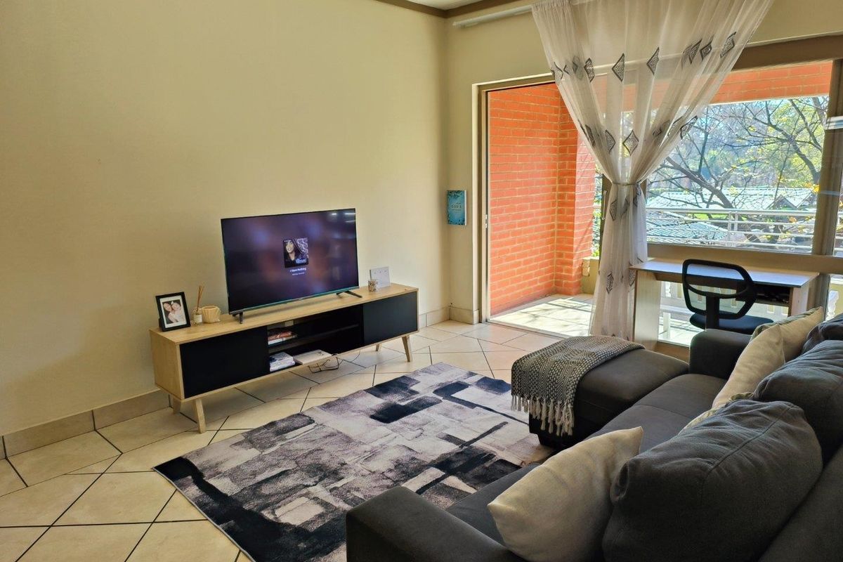 A comfortable living room featuring ceramic tiled flooring and a large sliding glass door that opens onto a private balcony with exposed brick walls.