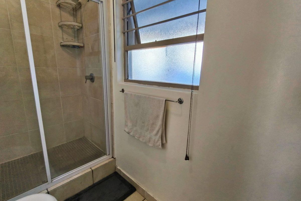 A functional bathroom featuring a tiled shower enclosure and a louvered window, providing basic utility and natural light.