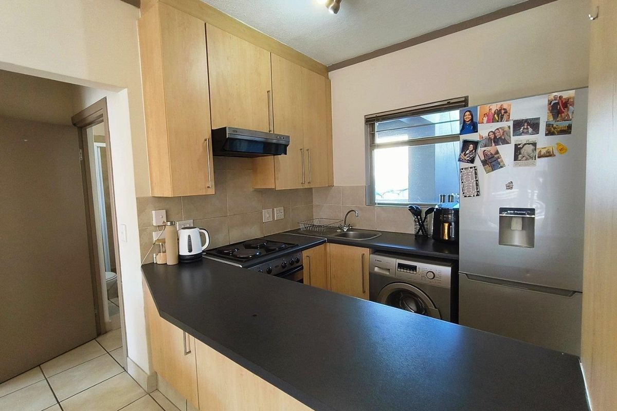 Compact kitchen featuring light wood cabinetry, dark countertops, tiled backsplash, and integrated appliance space, providing a functional layout for an apartment.
