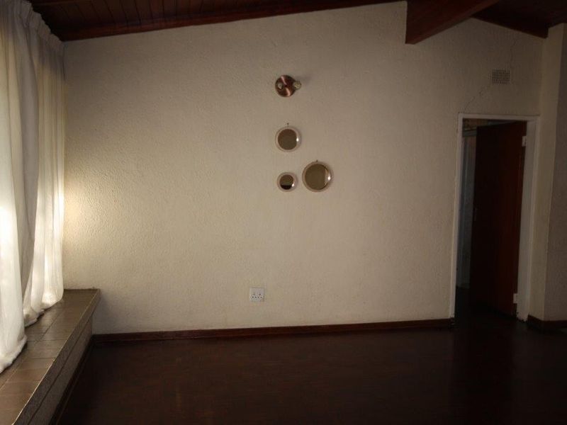 An empty living room featuring parquet flooring, exposed timber ceiling beams, and a tiled window ledge, offering a blank canvas for interior design.