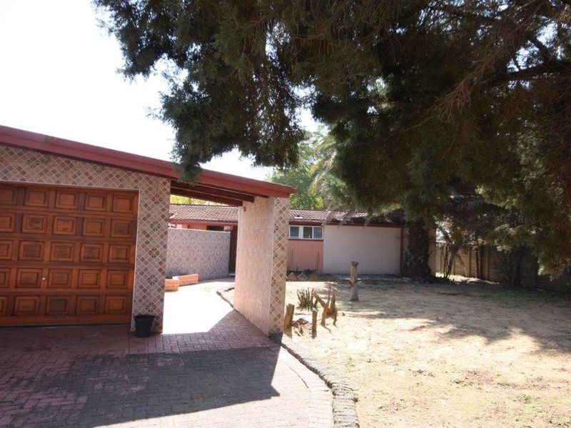 Front exterior view of the property featuring a garage, paved driveway, and covered entrance area with established trees and garden space.