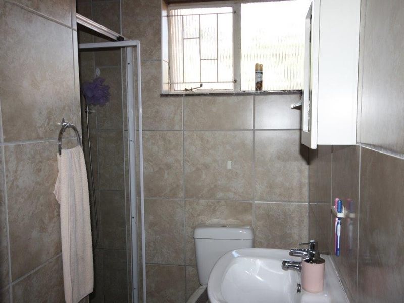 A functional bathroom featuring a shower enclosure, pedestal basin, toilet, and tiled walls with a window for natural light.