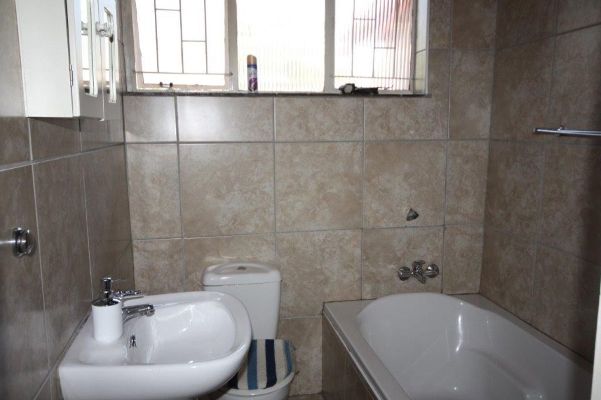 A functional bathroom featuring ceramic wall tiling, a pedestal basin, a built-in bathtub, and a toilet, with a window providing natural light.