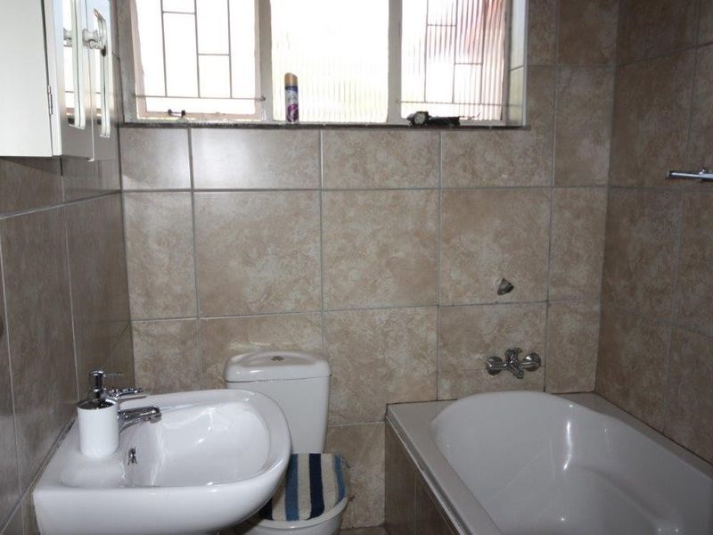 A functional bathroom featuring ceramic wall tiling, a pedestal basin, a built-in bathtub, and a toilet, with a window providing natural light.