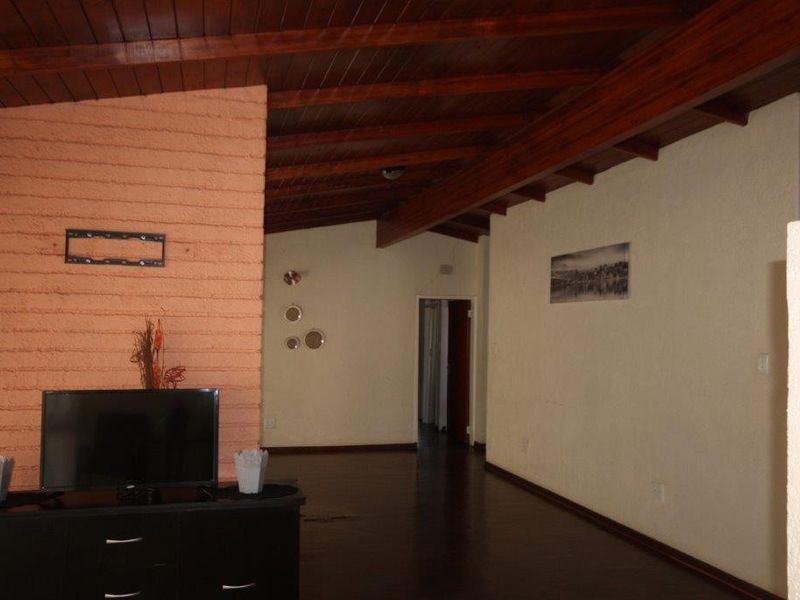 Spacious living area featuring a high exposed timber beam ceiling, dark wood flooring, and a prominent brick fireplace.
