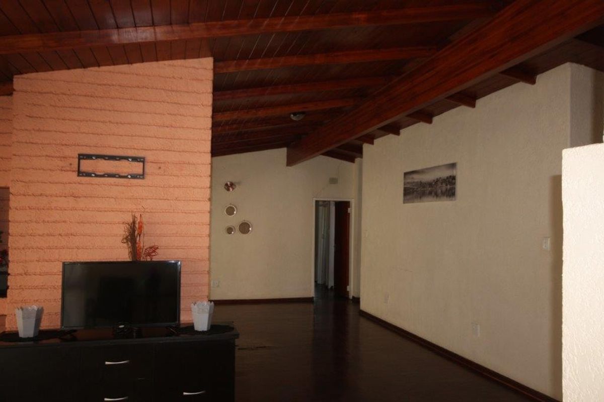Spacious living area featuring a high exposed timber beam ceiling, dark wood flooring, and a prominent brick fireplace.