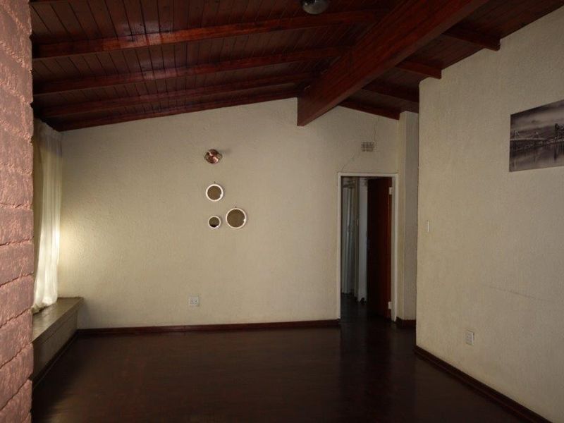 An empty living room featuring exposed timber beam ceilings, dark timber flooring, and a textured brick feature wall with a visible structural crack.