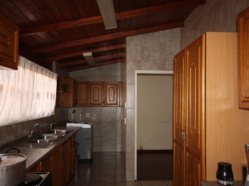 A functional kitchen featuring wooden cabinetry, tiled backsplash, and an exposed timber ceiling, offering a traditional aesthetic with ample storage space.