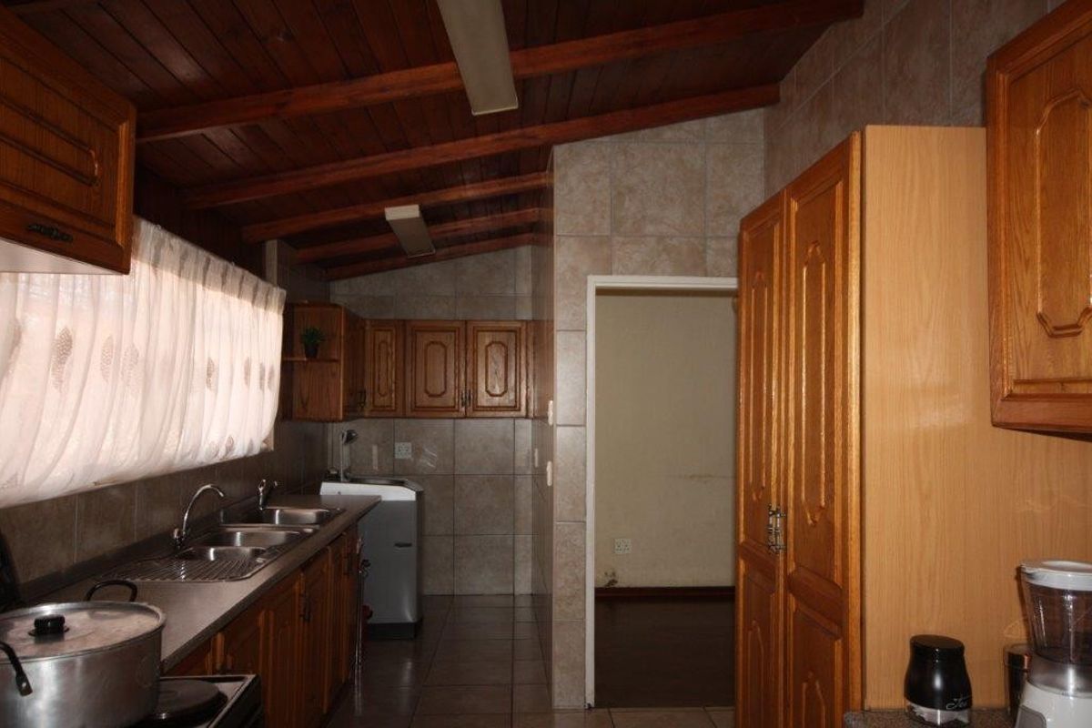 A functional kitchen featuring wooden cabinetry, tiled backsplash, and an exposed timber ceiling, offering a traditional aesthetic with ample storage space.