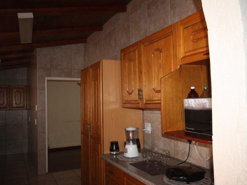 A kitchen featuring traditional wooden cabinetry, tiled backsplash, and an exposed timber beam ceiling, offering a functional layout with direct access to adjacent rooms.