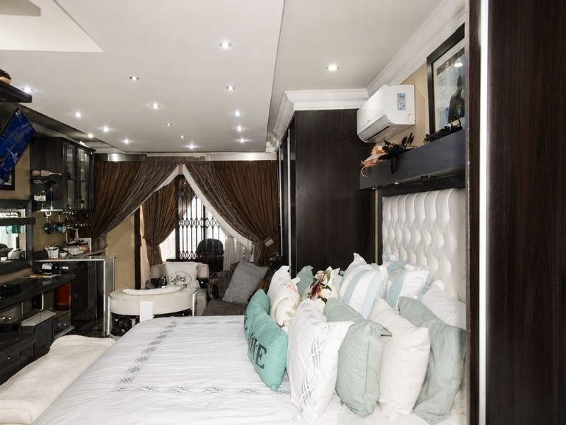 A well-appointed bedroom featuring built-in cabinetry, recessed downlighting, and a wall-mounted split-system air conditioner, with a security gate visible at the window.