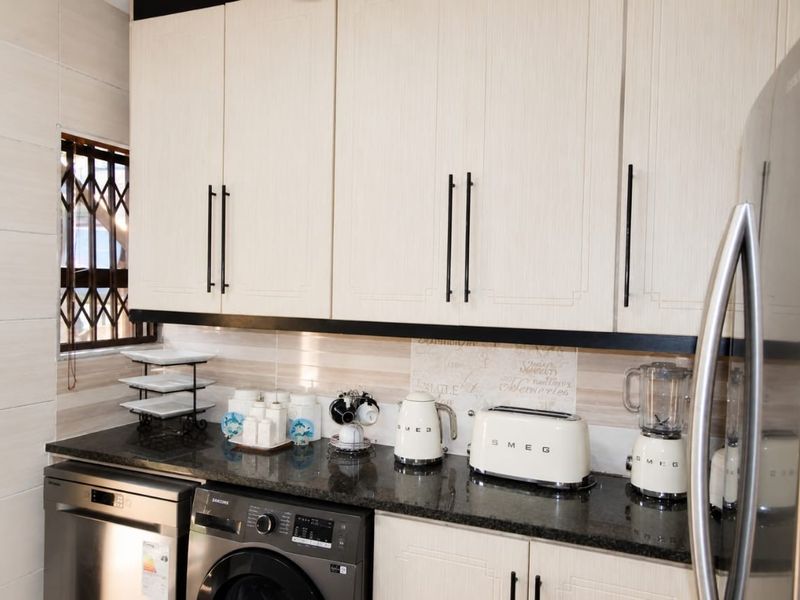 A well-maintained kitchen featuring light-toned cabinetry, dark granite countertops, a tiled backsplash, and integrated laundry and dishwashing appliances.
