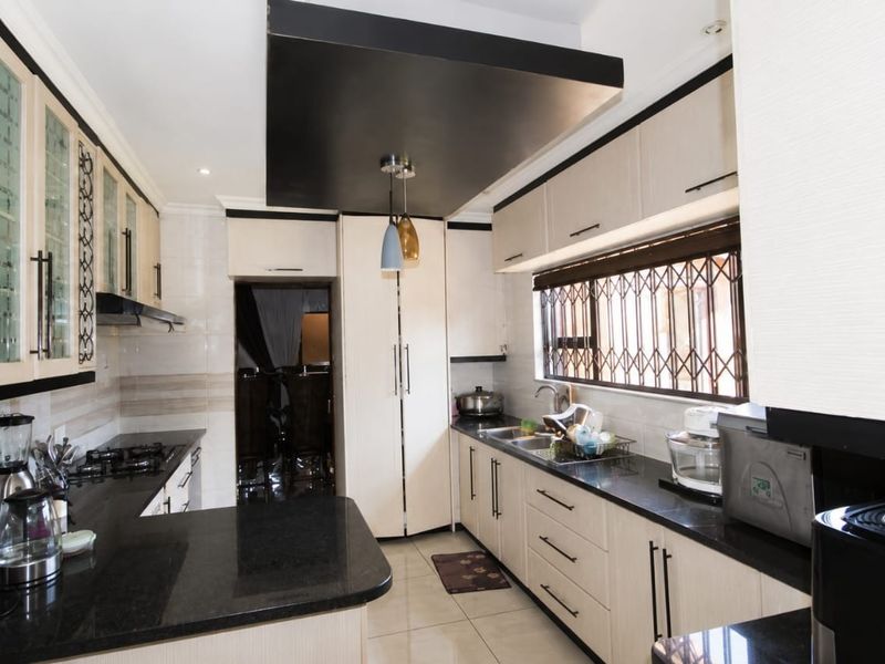 Modern kitchen featuring light wood cabinetry, contrasting black granite countertops, a gas hob, and a distinctive black drop ceiling feature.