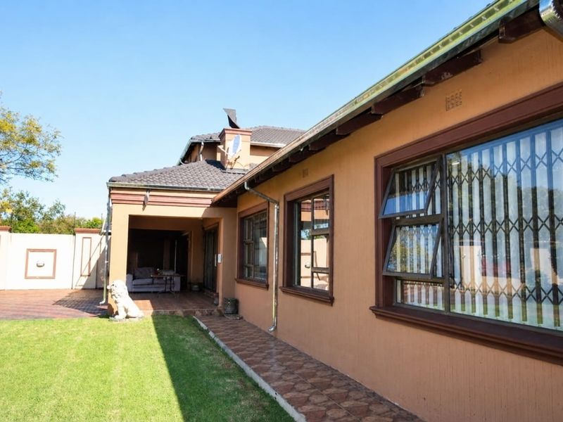 Rear view of the house featuring a covered patio, tiled walkway, and secure window fittings overlooking a well-maintained garden area.