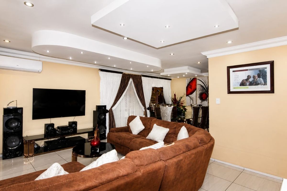 Spacious living room featuring a modern recessed ceiling with integrated downlights, tiled flooring, and a wall-mounted air conditioning unit.
