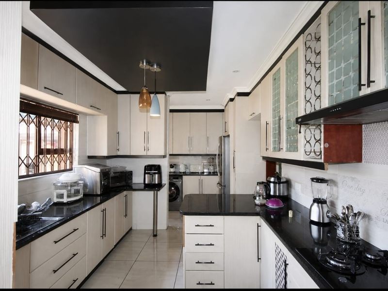 Modern kitchen featuring sleek built-in cabinetry, contrasting black granite countertops, a gas hob, extractor fan, and stylish tiled flooring.