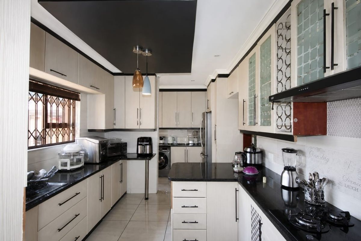 Modern kitchen featuring sleek built-in cabinetry, contrasting black granite countertops, a gas hob, extractor fan, and stylish tiled flooring.