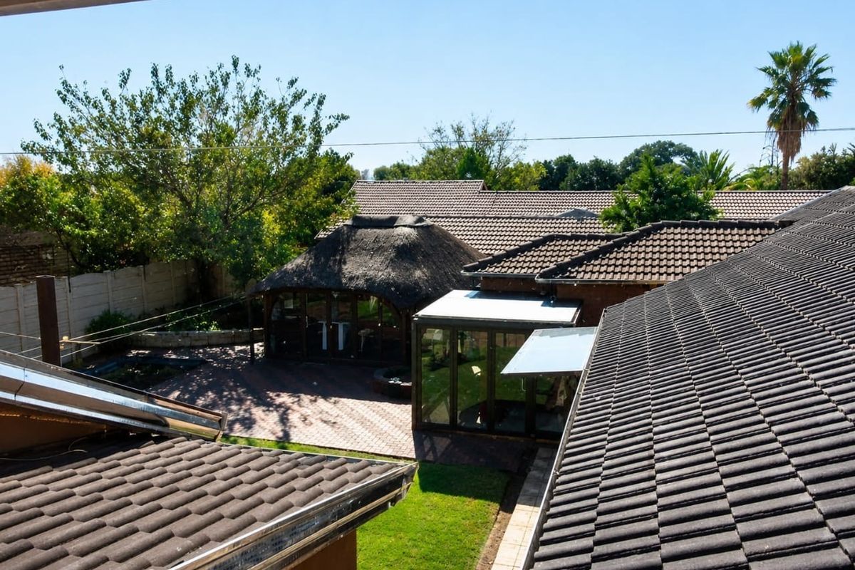 Aerial view of the property backyard featuring a thatched lapa, paved patio area, and a glass-enclosed sunroom extension.