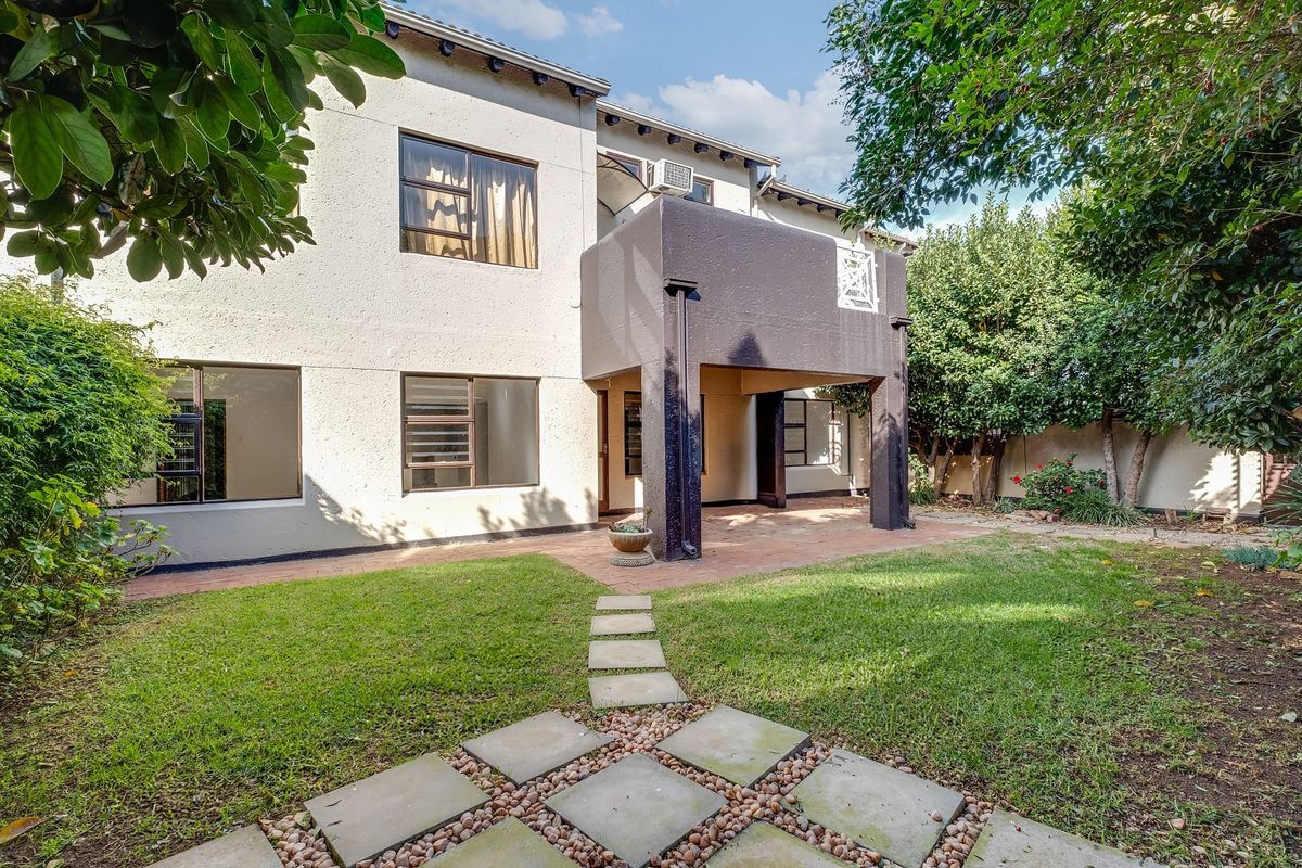 Rear view of the townhouse featuring a covered patio area, paved walkway, and a private garden space.