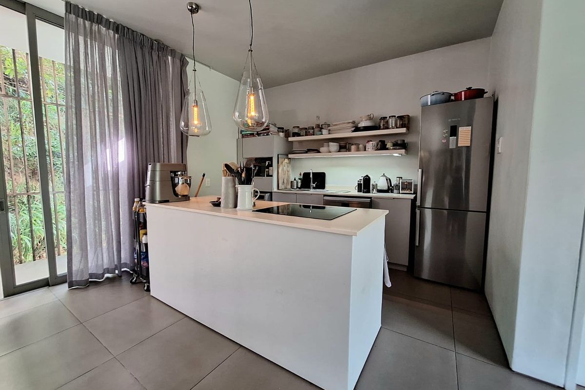Modern kitchen featuring a central island with a built-in induction hob, sleek cabinetry, open shelving, and large sliding glass doors leading to the exterior.