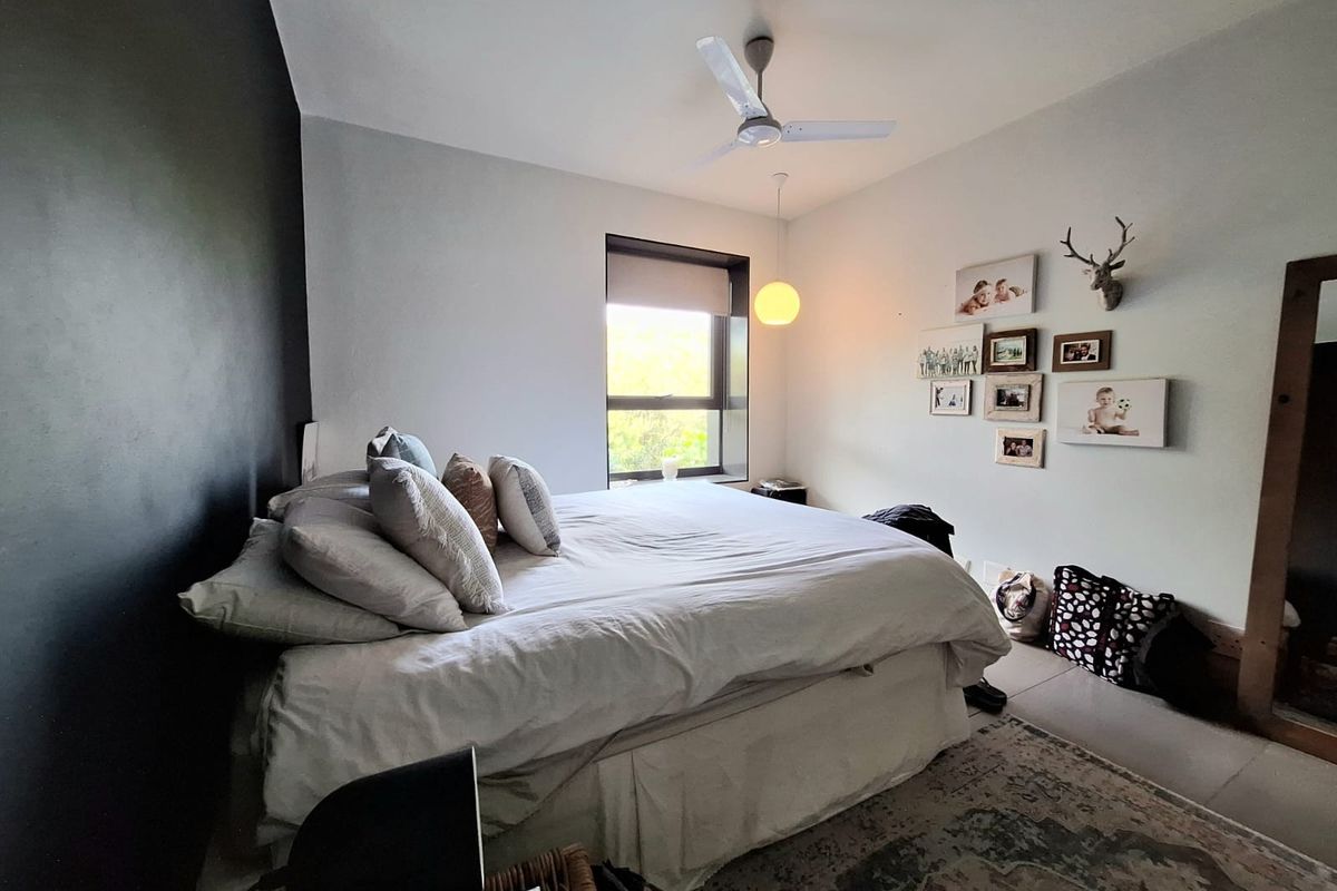 A well-lit bedroom featuring a ceiling fan, a large window with natural light, and a modern accent wall.
