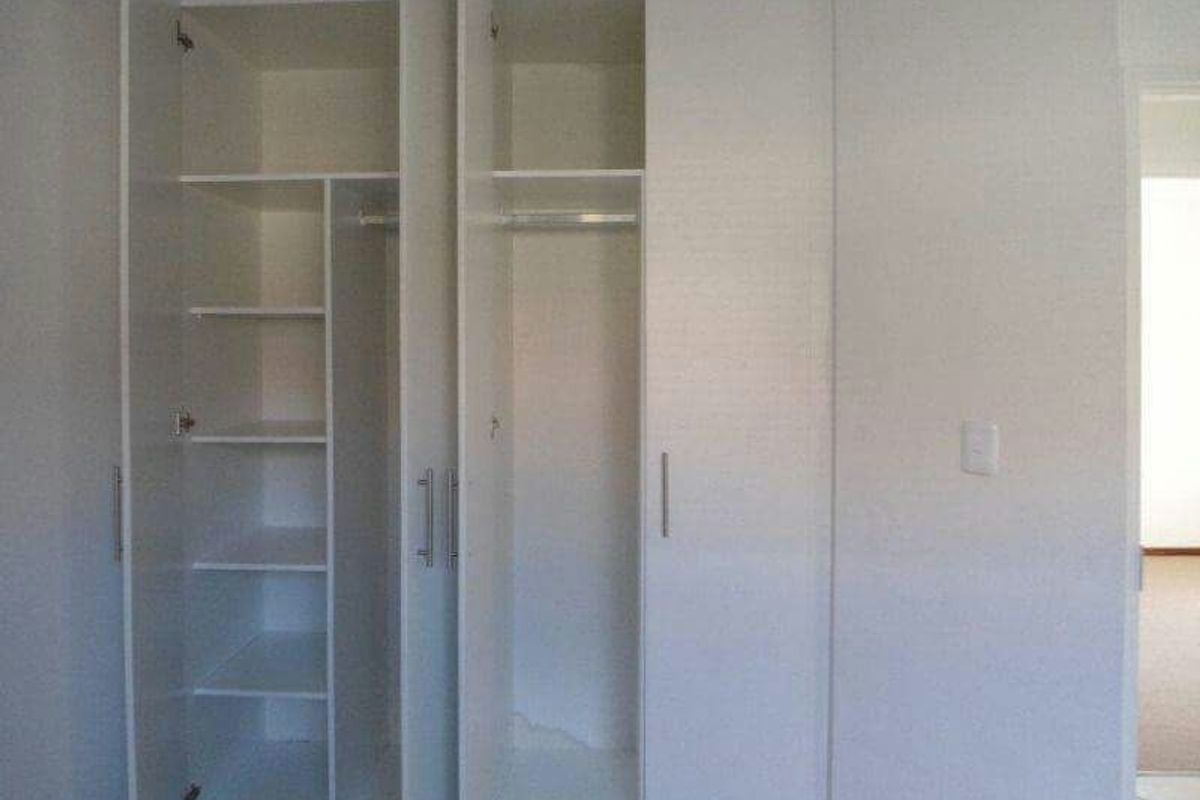 A bedroom featuring built-in white cabinetry with integrated shelving and hanging space, providing ample storage solutions.