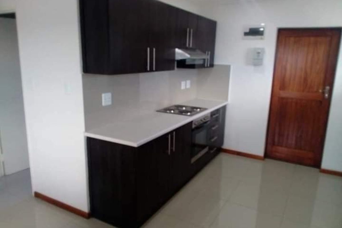 Modern kitchen featuring dark cabinetry, light countertops, a built-in oven, hob, and extractor fan, complemented by tiled flooring.