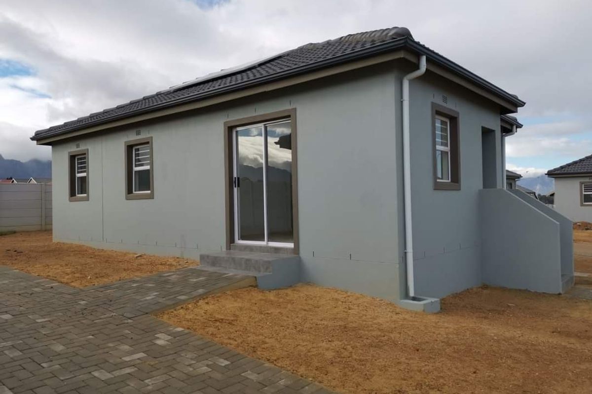 A modern single-story house exterior featuring grey rendered walls, dark tiled roof, sliding glass door, and paved walkway access.