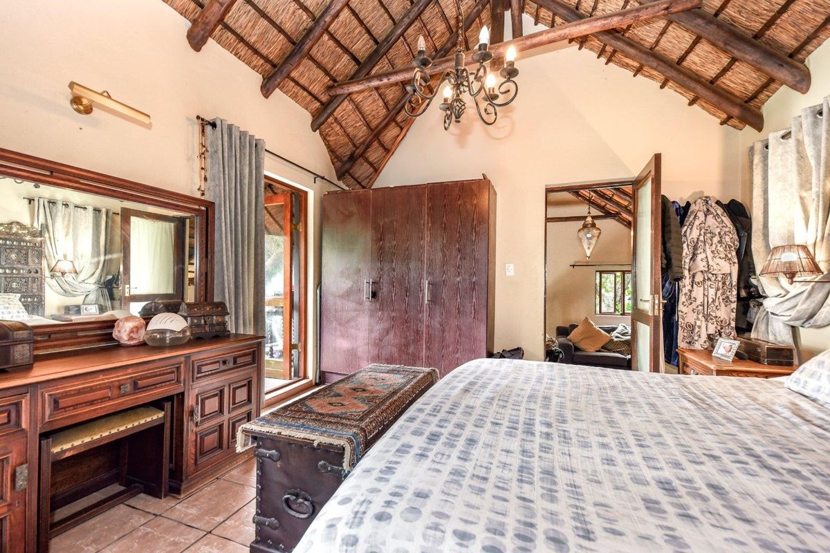 Spacious bedroom featuring a high vaulted thatch ceiling with exposed timber beams, tiled flooring, and built-in wooden cabinetry.
