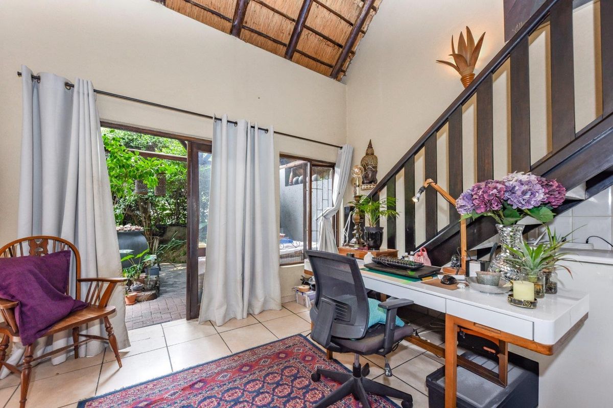 A versatile living space featuring a high thatched ceiling, tiled flooring, and direct access to a private patio area via sliding glass doors.