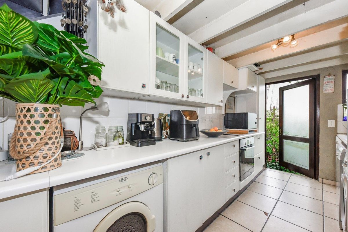 A functional galley-style kitchen featuring white cabinetry, integrated oven, and direct access to the rear exterior.