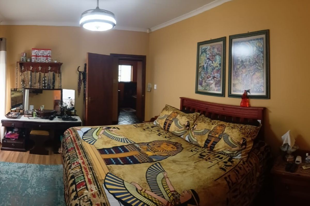 A spacious bedroom featuring laminate flooring, an integrated air conditioning unit, and a ceiling fan, with direct access to an adjoining room.