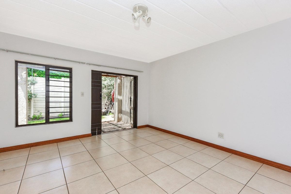 A bright, empty living room featuring tiled flooring, a ceiling-mounted light fixture, and direct access to an outdoor patio area through a sliding door.