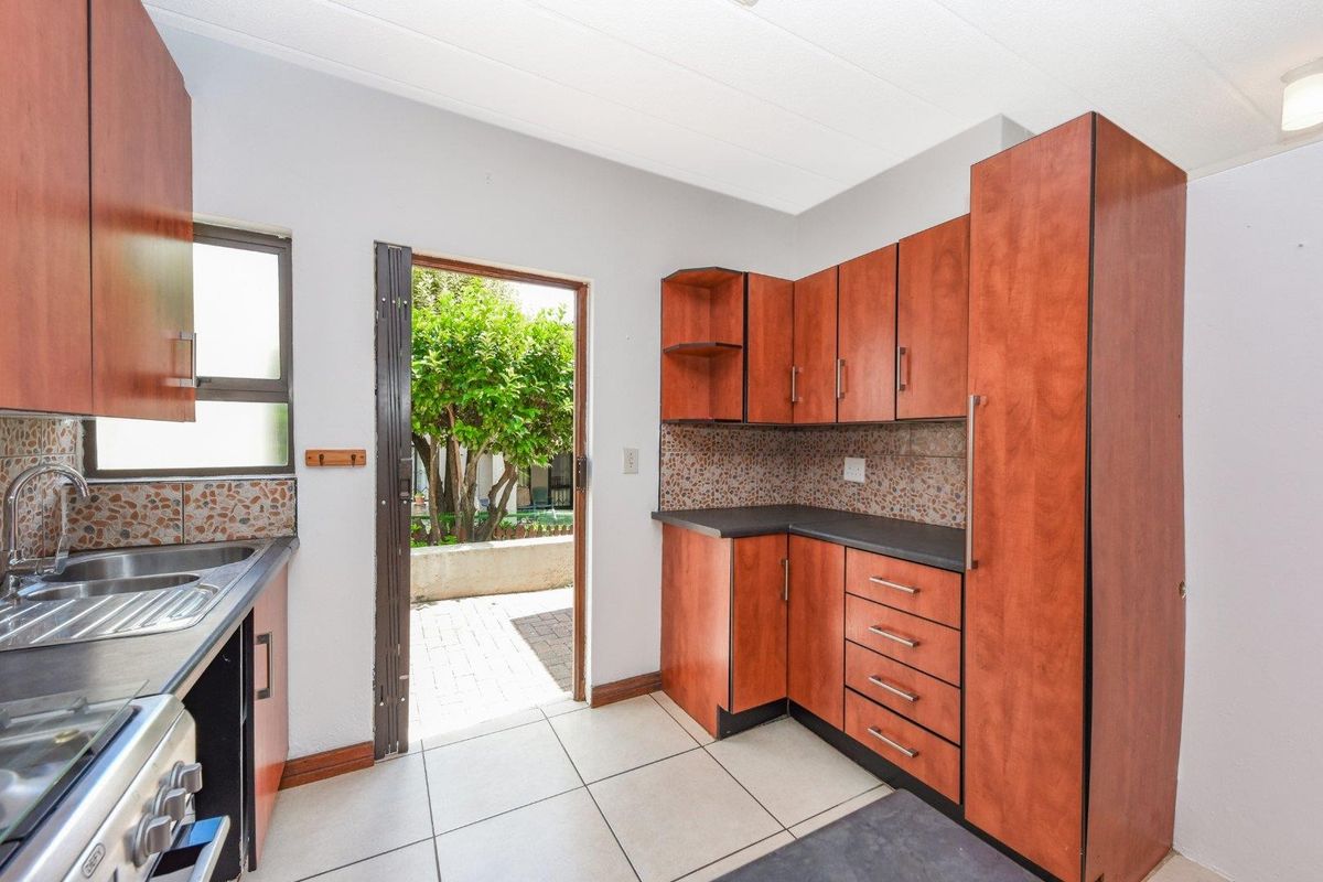 A functional kitchen featuring wood-look cabinetry, dark countertops, tiled flooring, and direct access to an outdoor patio area.