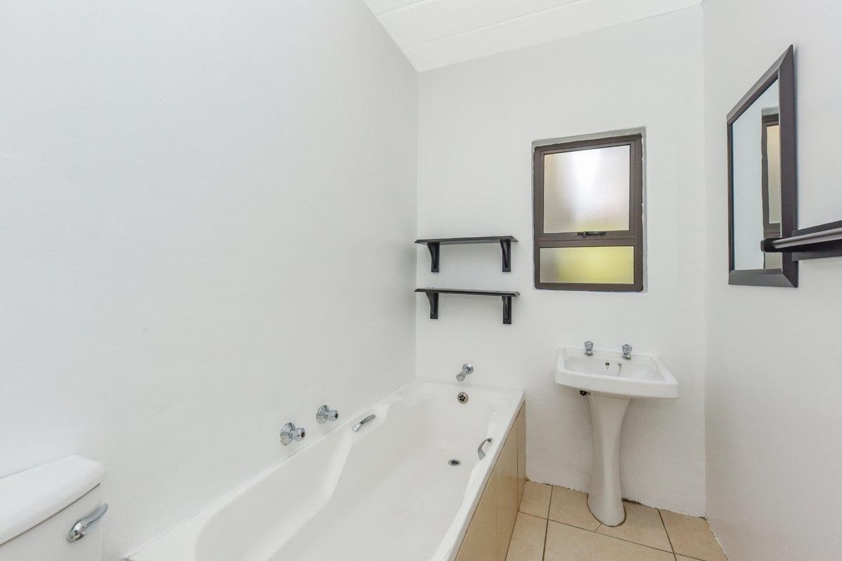 A functional bathroom featuring a pedestal basin, a built-in bathtub with chrome fixtures, and a small frosted glass window.