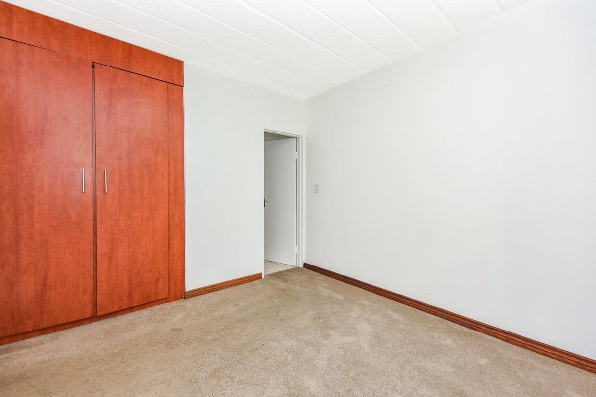 A clean, empty bedroom featuring neutral carpeting, white walls, and a built-in wooden wardrobe with double doors.