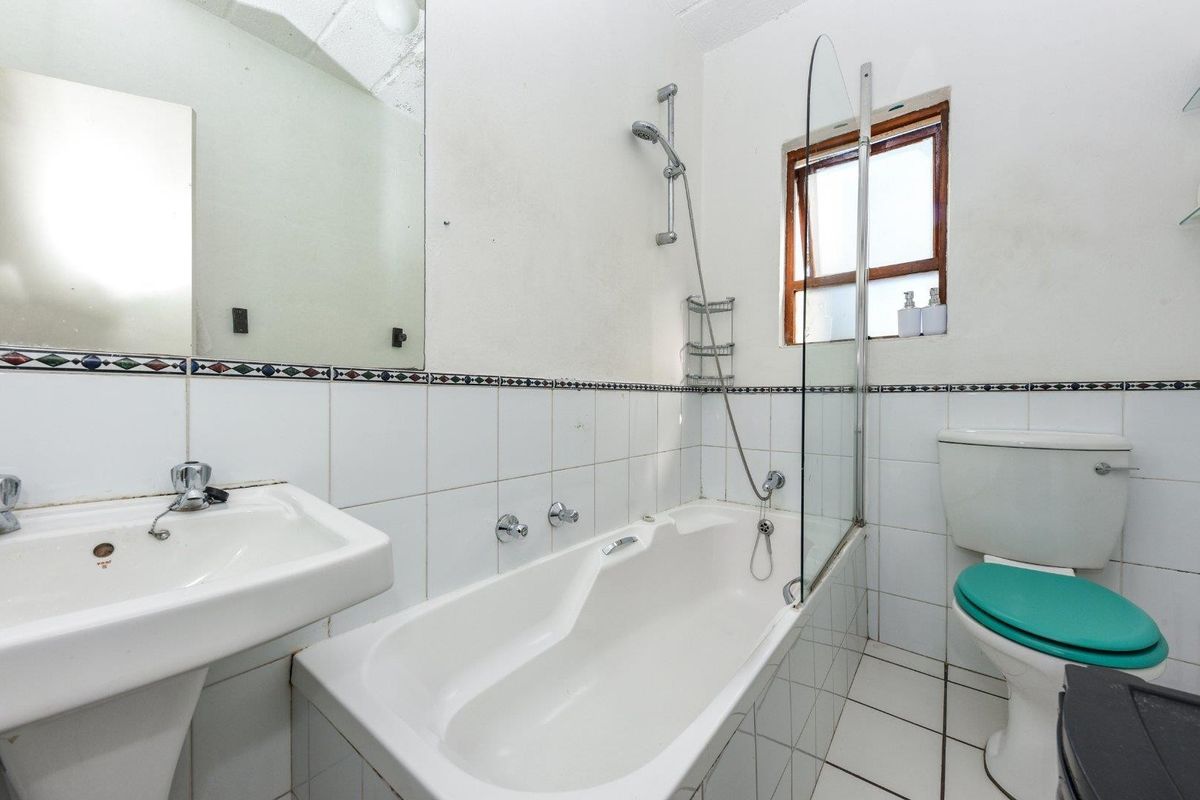 A dated bathroom featuring a white bathtub with a glass shower screen, pedestal basin, and toilet, finished with white wall tiles and a decorative border.