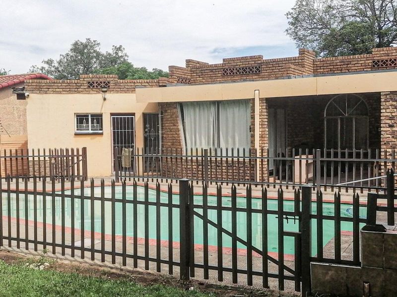 Rear exterior view featuring a swimming pool enclosed by metal fencing, adjacent to a covered patio and brick-finished house structure.
