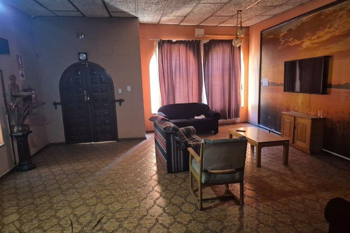 Spacious living room featuring an arched double door entrance, textured ceiling tiles, and patterned vinyl flooring, offering a dated aesthetic ready for modernization.